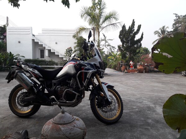 Una motocicleta estacionada en una entrada con un edificio blanco y palmeras al fondo.