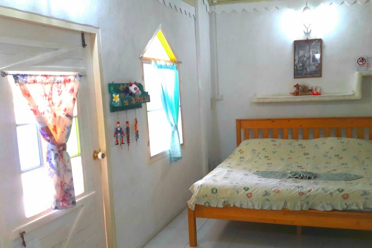 A bedroom with a wooden bed, a window with curtains, a wall-mounted shelf, and a door.