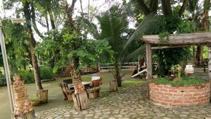 Un patio empedrado con mesas y bancos de madera rústica, rodeado de abundante vegetación y una jardinera de ladrillo.