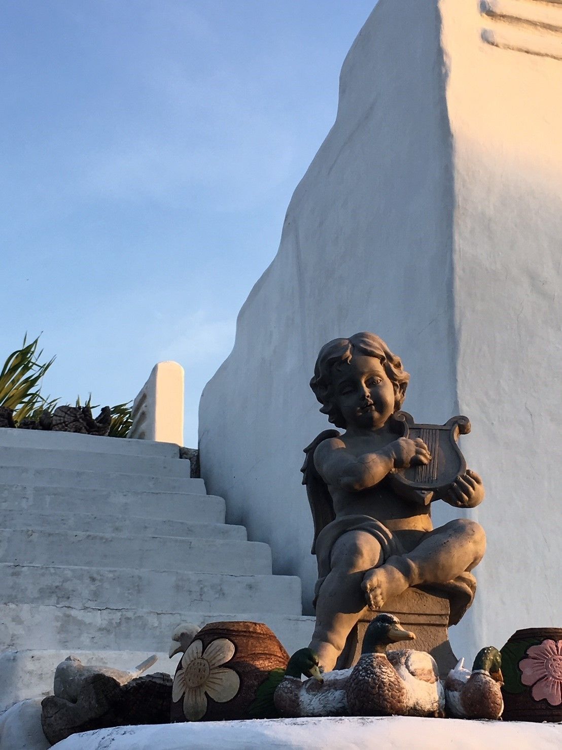 Una estatua de un niño tocando una lira, frente a una pared blanca con una escalera que sube.