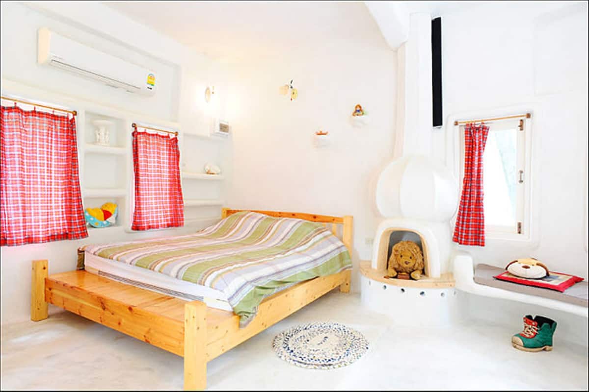 A cozy bedroom with a wooden bed, red checkered curtains, a small shelf with toys, and a window with a red curtain.