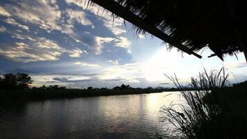 Una vista tranquila de un lago, con una estructura de techo de paja, agua calma y un cielo parcialmente nublado.
