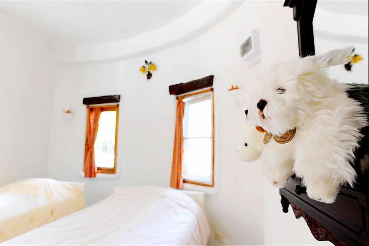 A bedroom with two beds, a window with orange curtains, and a white wall with a small decorative item.
