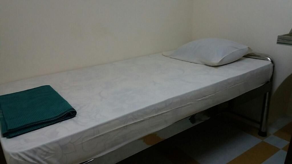 Habitación individual con una cama blanca, un edredón verde doblado y una almohada blanca.