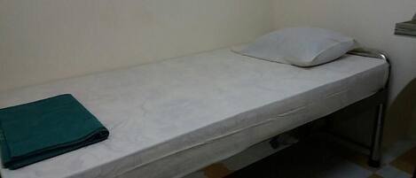 Habitación individual con una cama blanca, un edredón verde doblado y una almohada blanca.