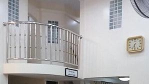 Un comedor con techo alto, balcón, reloj y escalera que sube a un nivel superior.