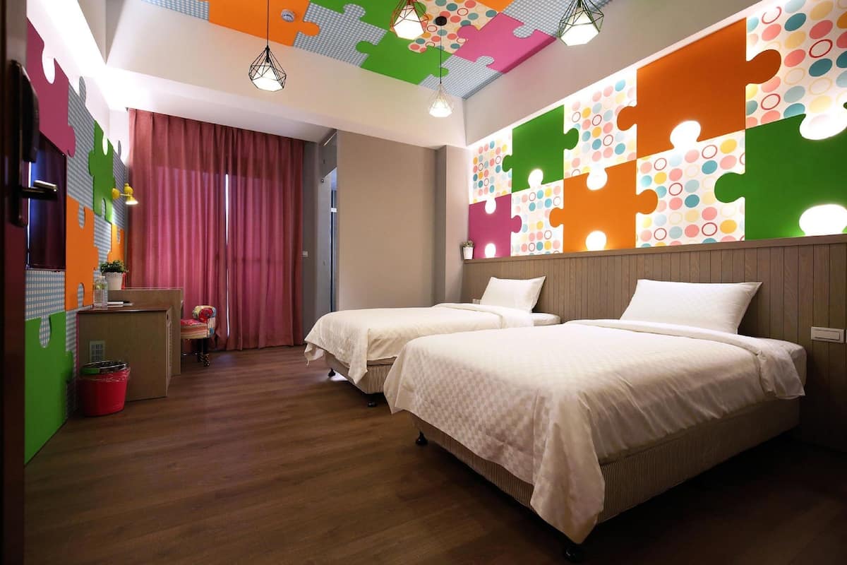 Habitación de hotel con dos camas, piso de madera, escritorio con silla y pared con diseño de puzzle.