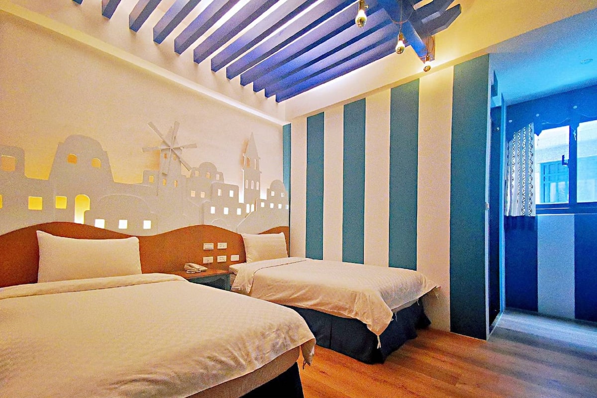 Habitación de hotel con dos camas, piso de madera, un mural con vista a la ciudad y una ventana con cortinas.