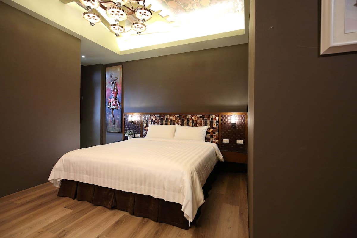 Un dormitorio moderno con una cama grande, una lámpara decorativa en el techo y un cuadro de un paisaje urbano en la pared.
