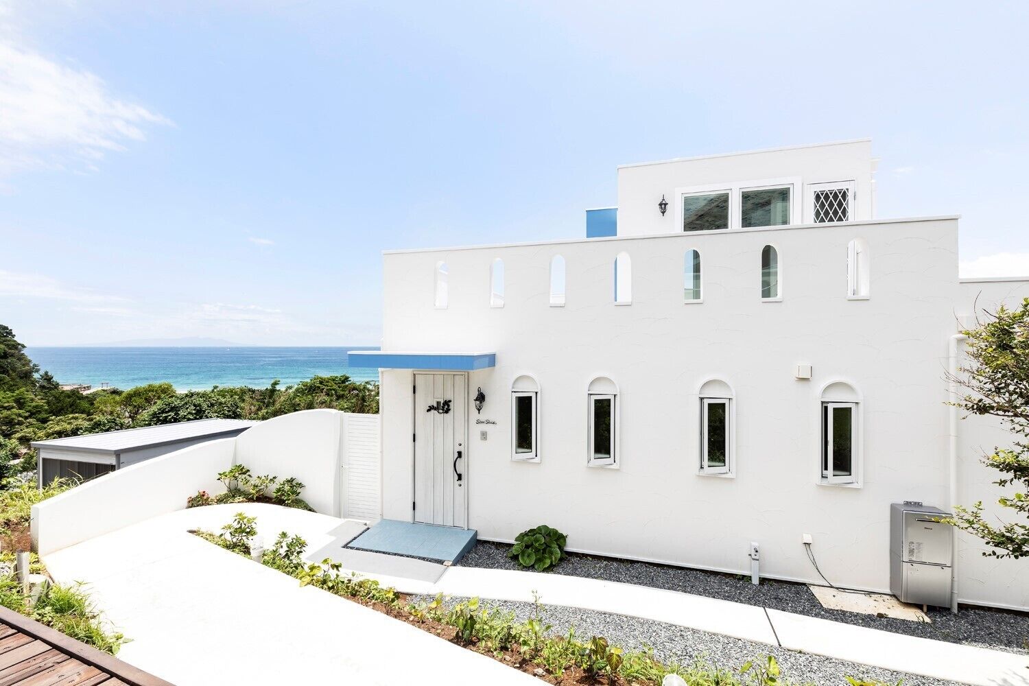 Un edificio moderno blanco con entrada azul, un porche pequeño y vista al océano.