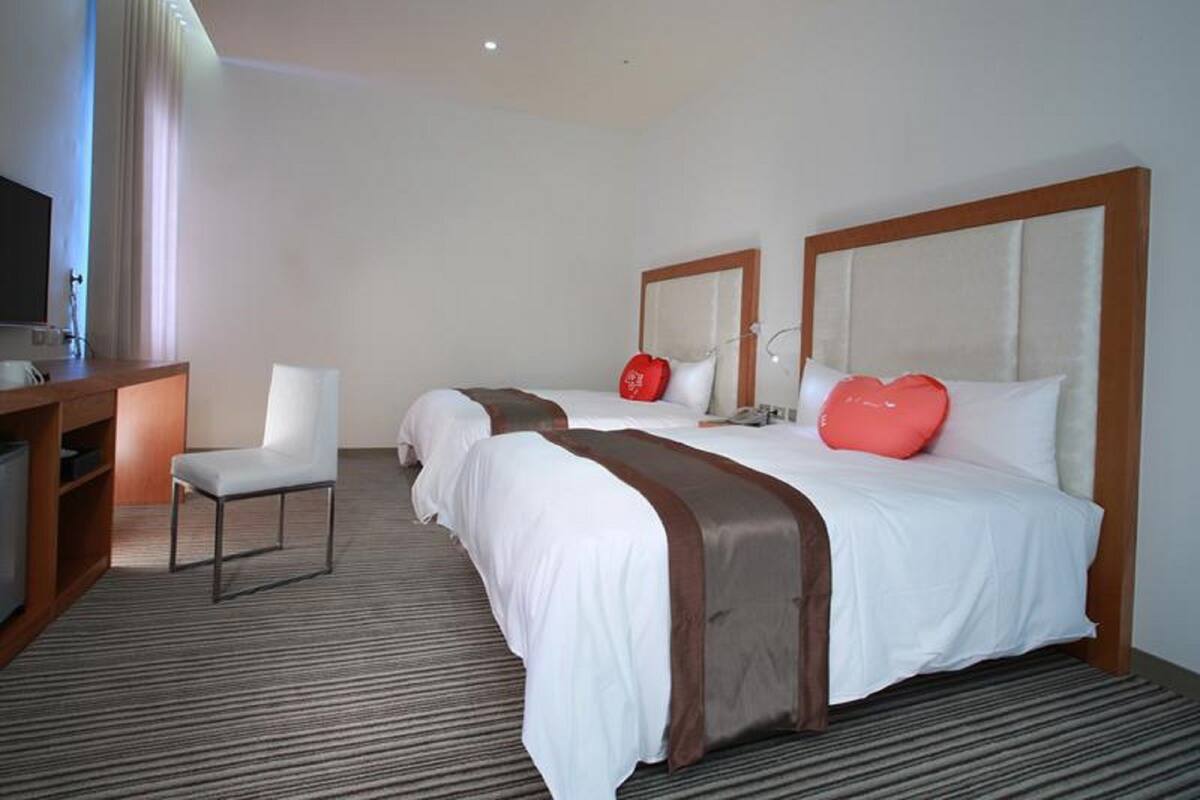 A hotel room with two beds, a desk, a chair, and a television.
