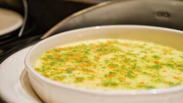 A white bowl of soup with green and orange specks on a white plate.