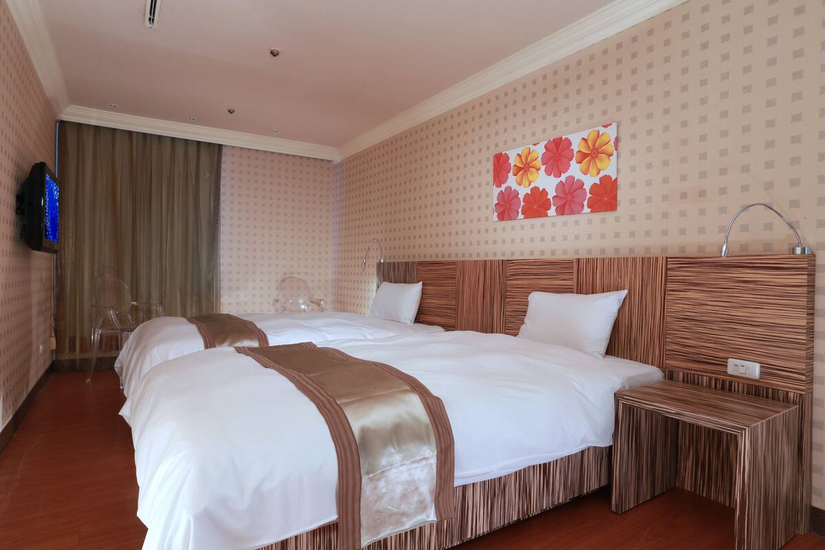 A hotel room with two beds, a TV, a painting, and a mirror.