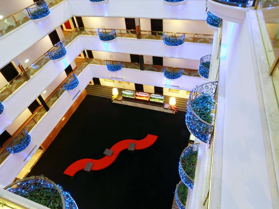 A multi-level atrium with a central red seating area, glass railings, and decorative blue hanging baskets.