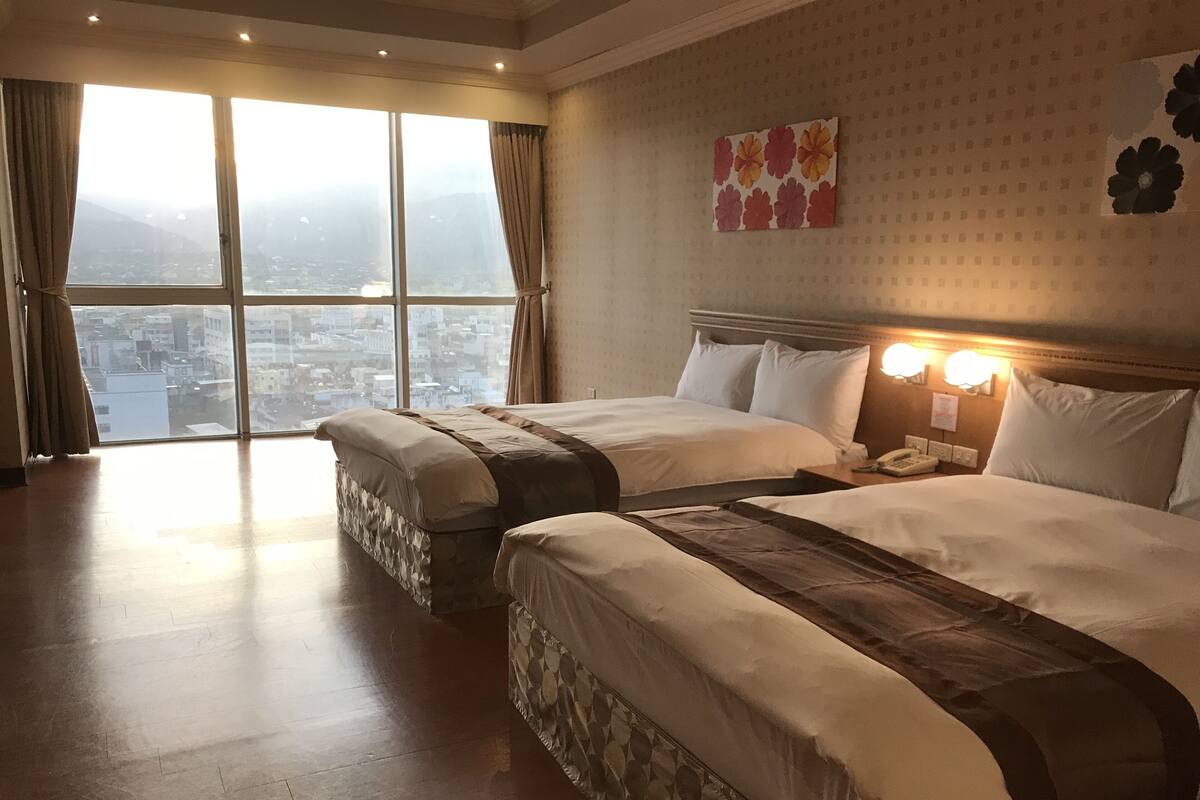 A hotel room with two beds, a city view, a patterned wall, and a nightstand with a phone.