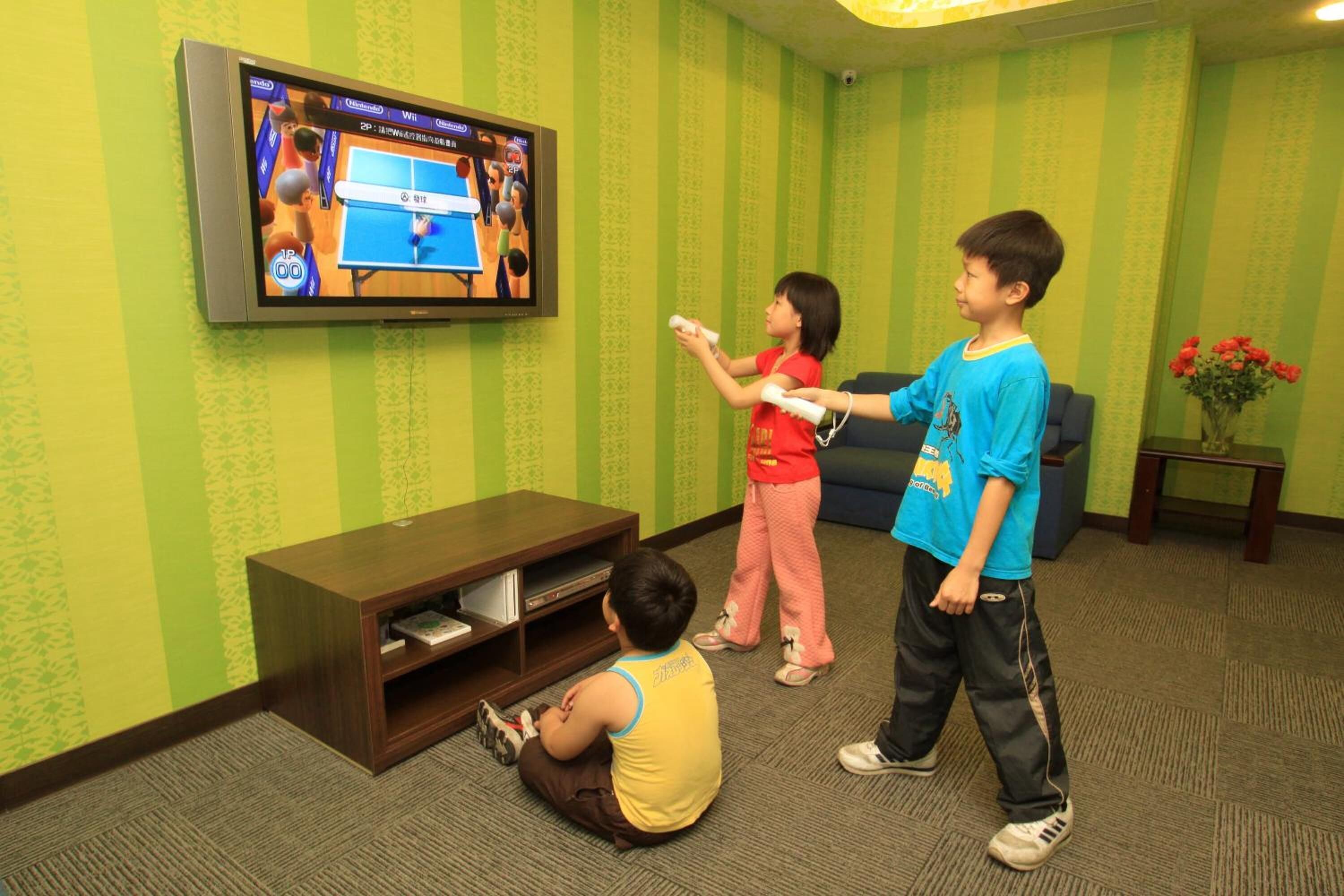 A living room with a television displaying a video game, a sofa, a small table with a vase, and a carpeted floor.