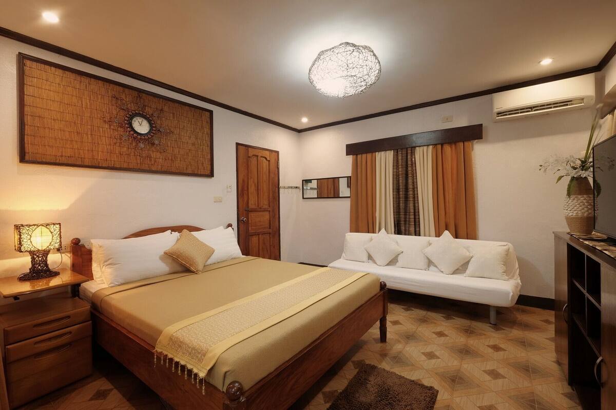 A bedroom with a bed, bedside table, lamp, sofa, and a decorative wall piece.