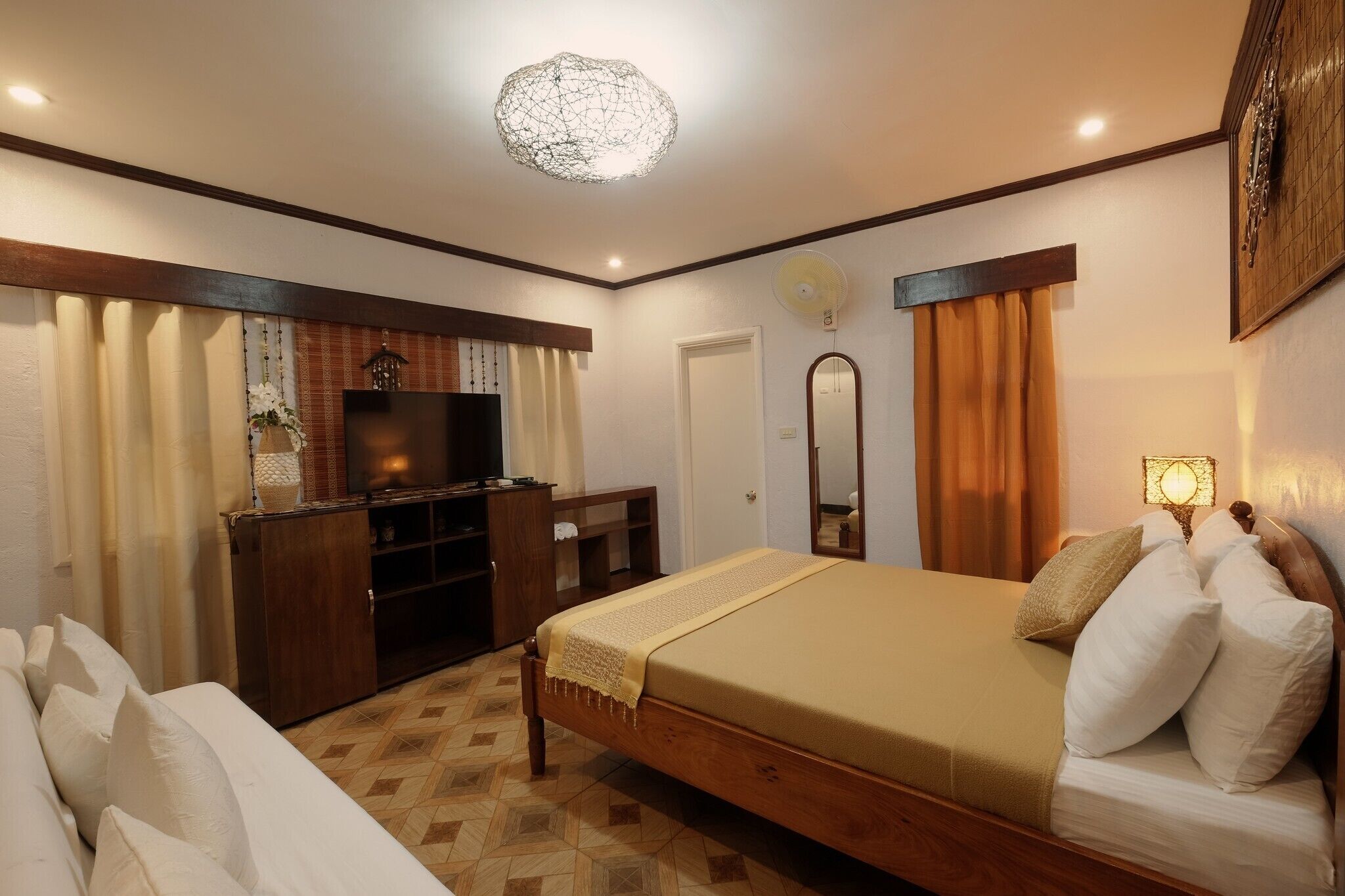 Un dormitorio ordenado con cama, cómoda, televisor y espejo.