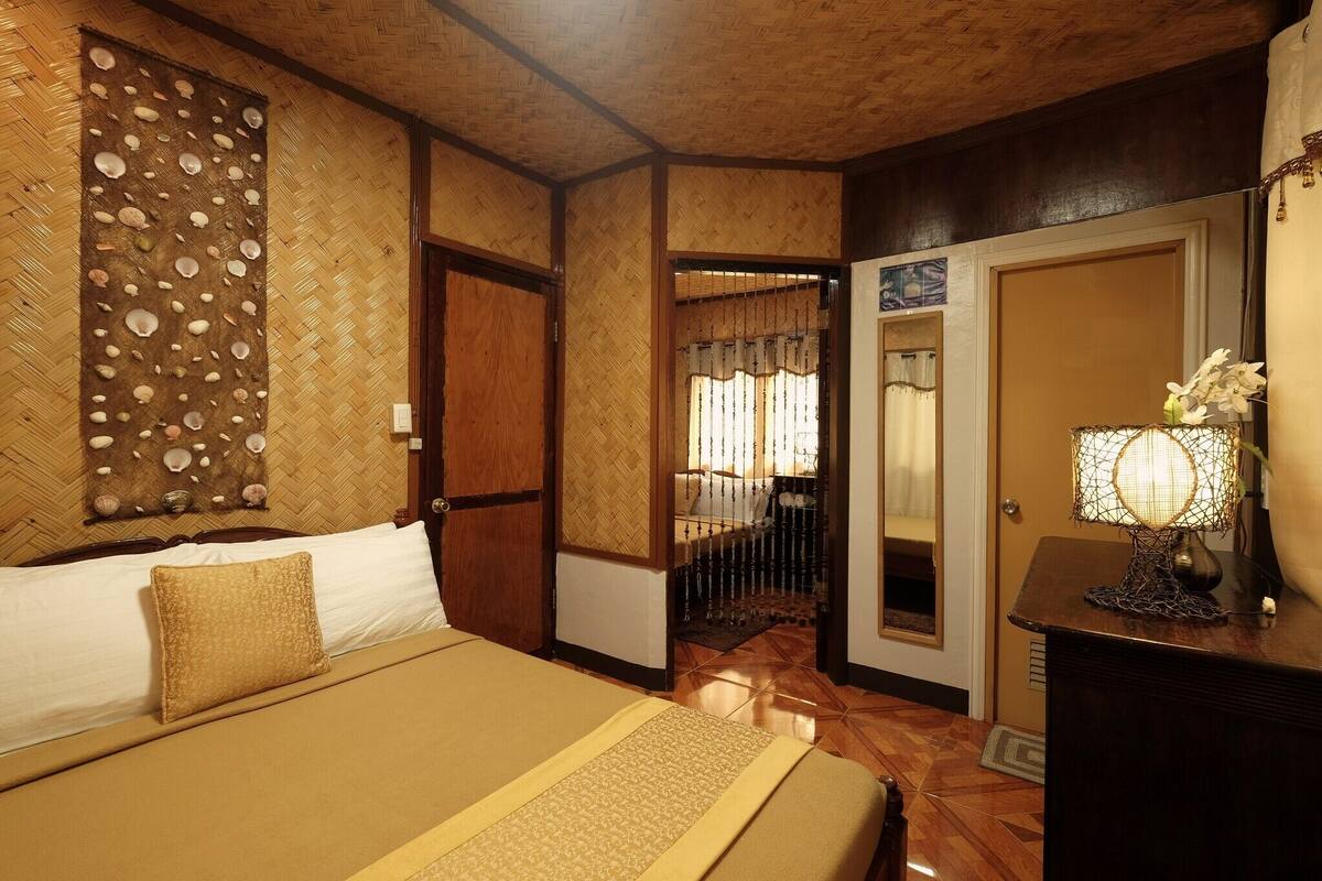 A hotel room with a bed, a wooden headboard, a wall with a shell pattern, a door, and a nightstand with a lamp.