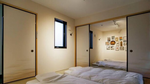 A minimalist hotel room with two beds, a large mirror, and a wall adorned with framed pictures. - Shukusai Art stay in Tofukuji (Kyoto)