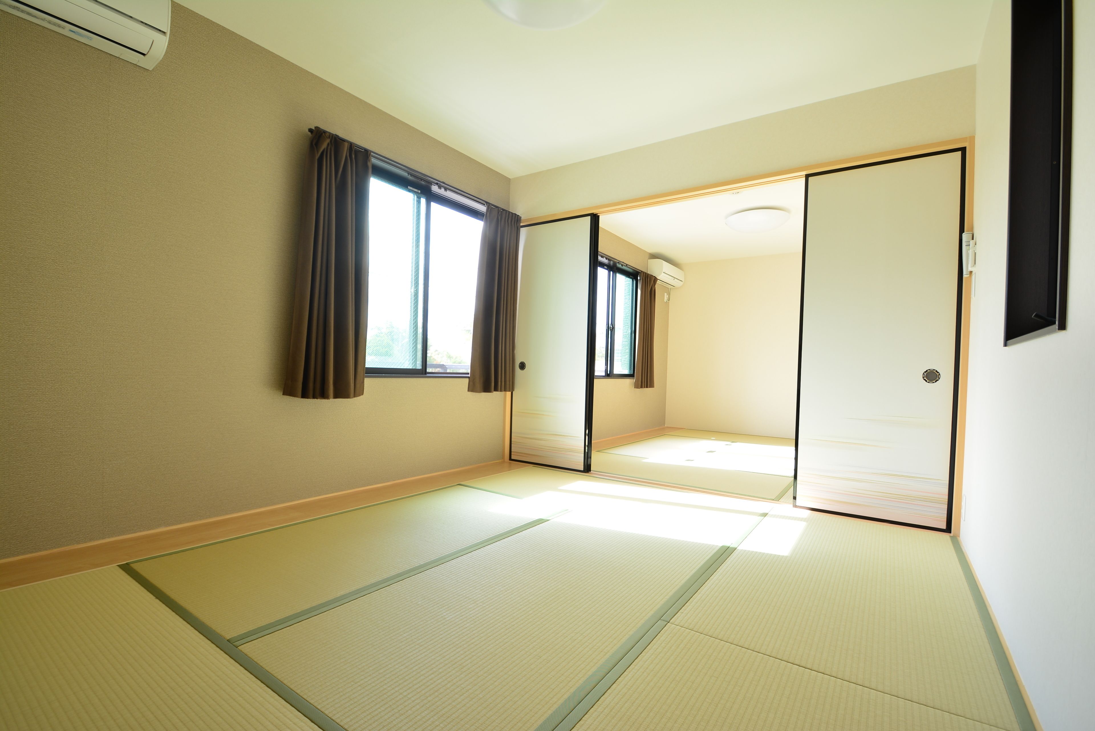 A room with tatami mats, sliding doors, and a large window with curtains.