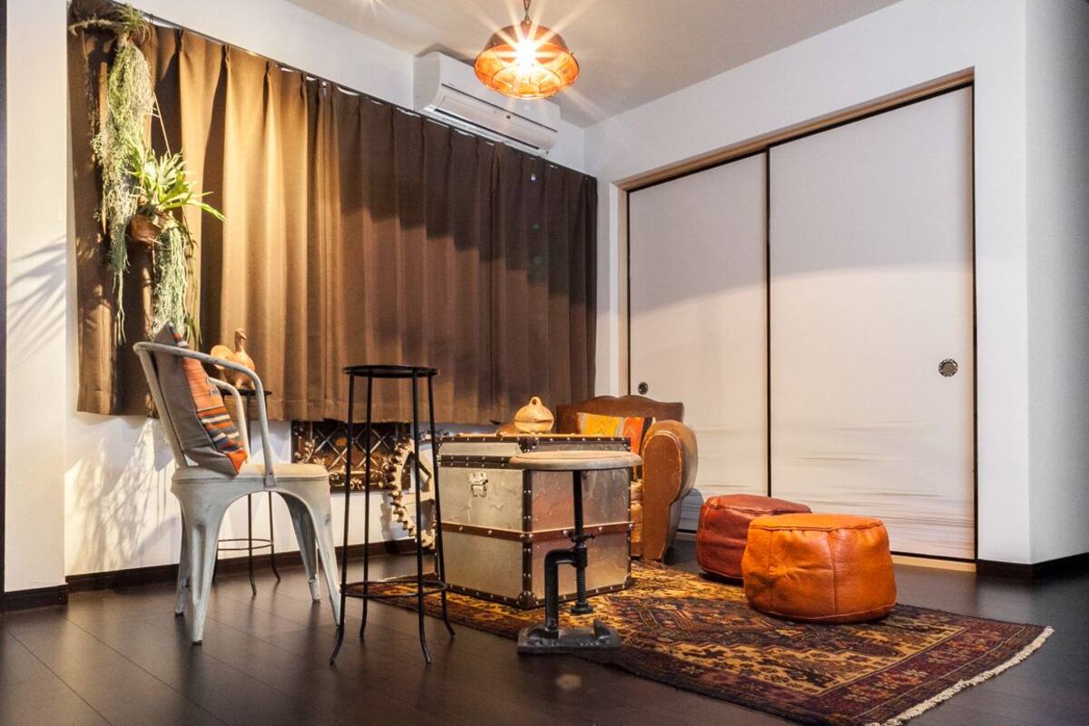 A room with a large wardrobe, a dining table with chairs, a sofa, and a patterned rug.