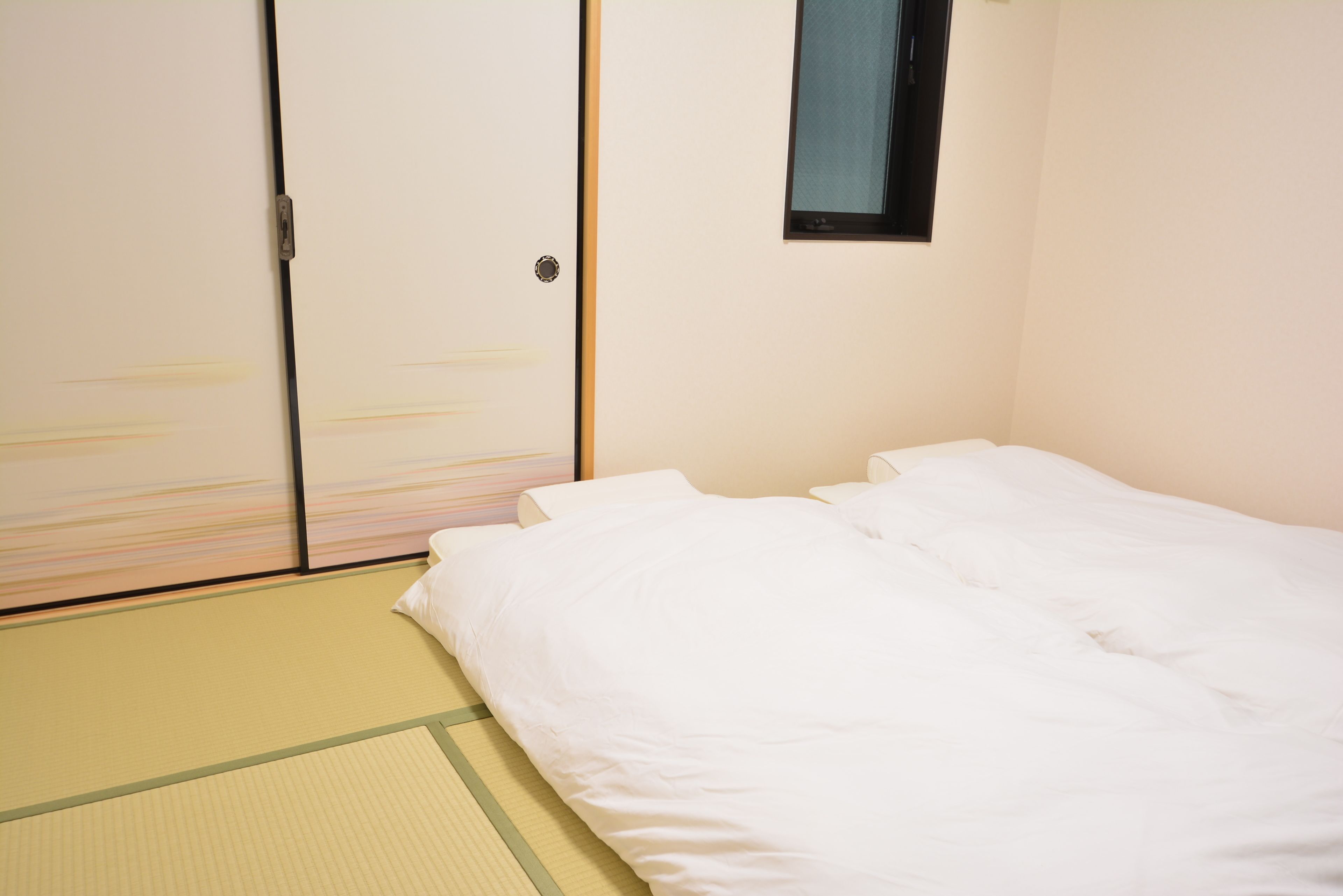 A room with tatami mat flooring, a bed with white bedding, and a sliding door with a small window.