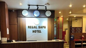 Mostrador de recepción en el Hotel Regal Sapa, con relojes encima, mostradores de registro y un mostrador de salida.