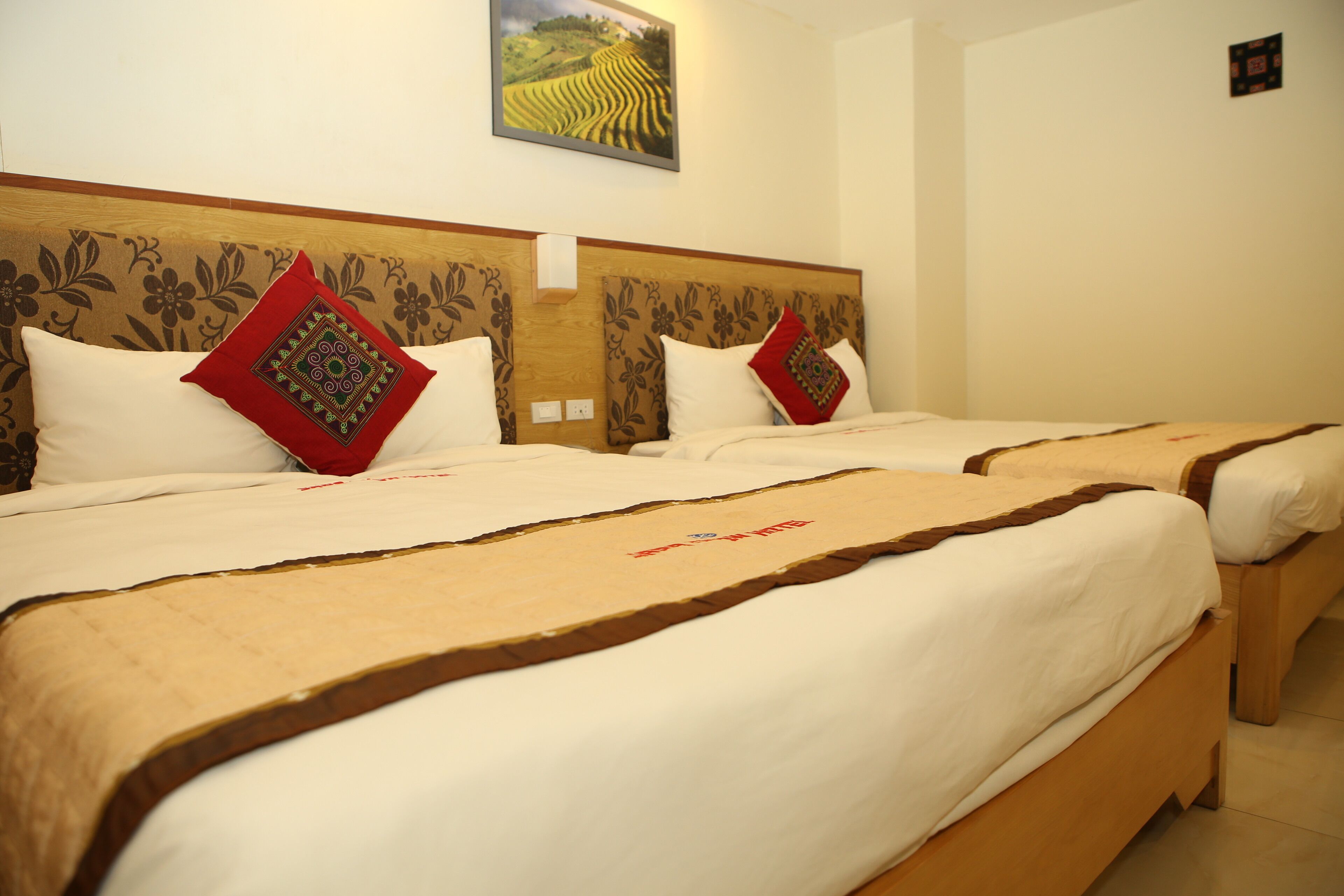 Two double beds with wooden headboards, white bedding, and red decorative pillows.