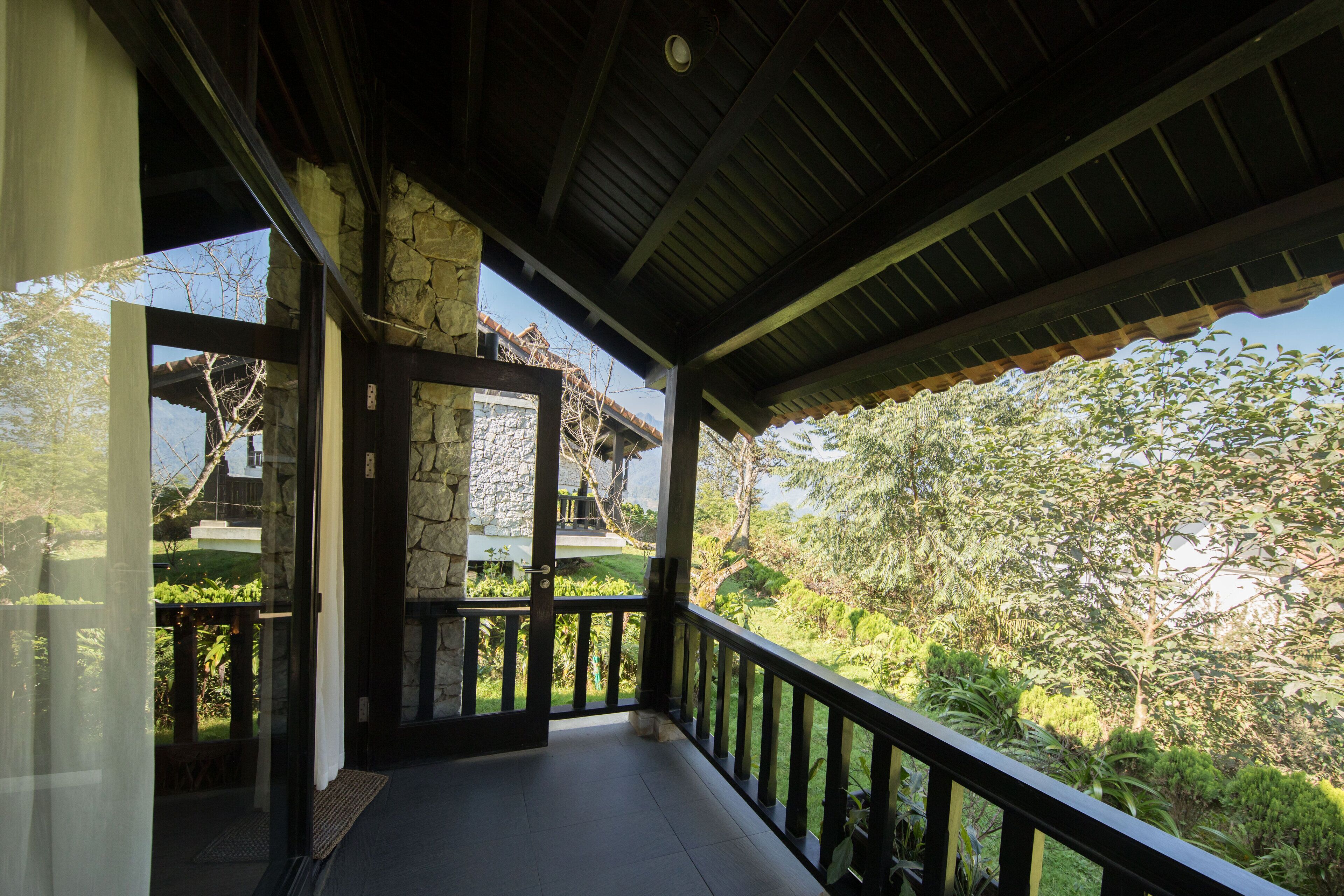 A covered balcony with stone walls and a view of lush greenery.