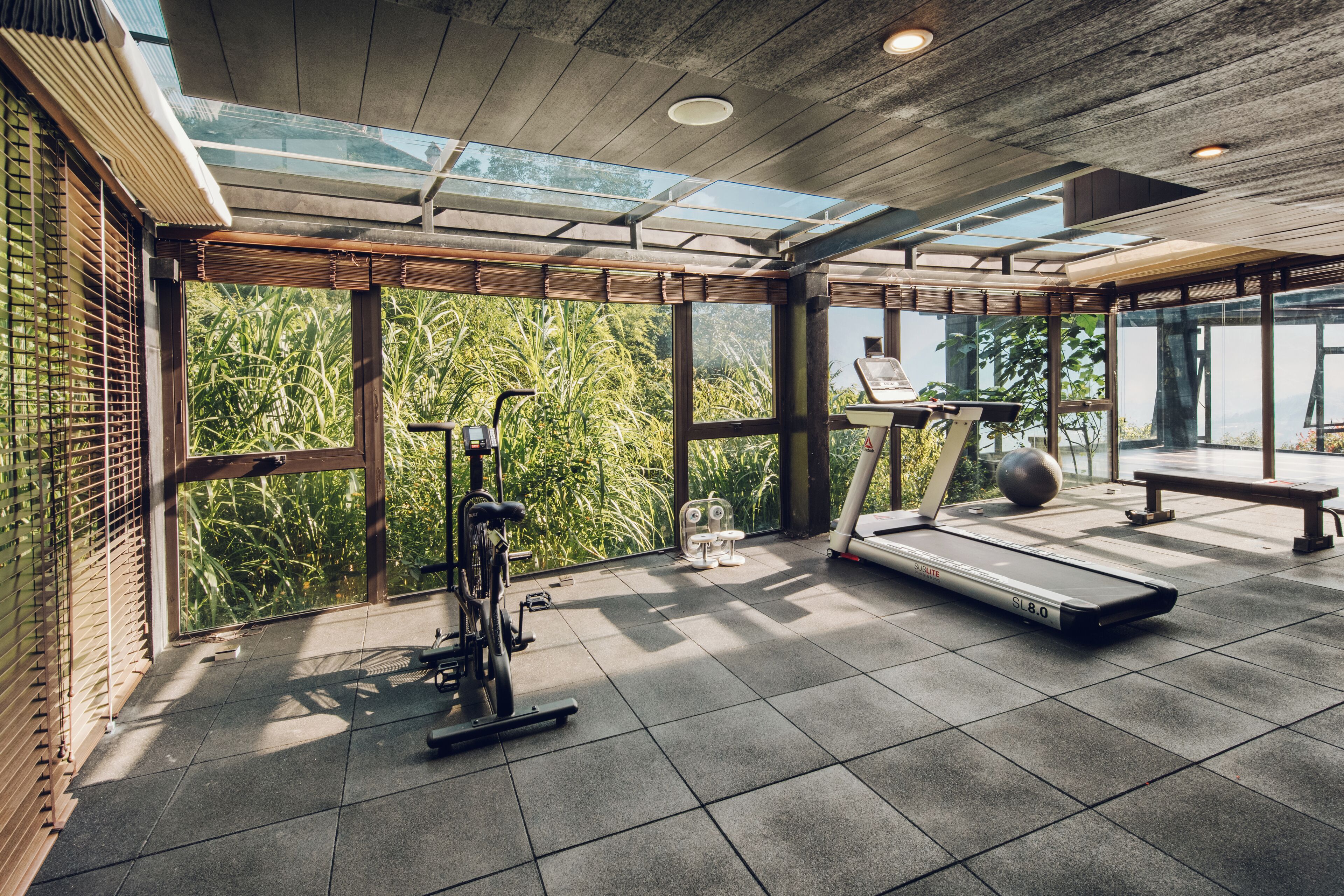 Ein Fitnessraum mit Trainingsgeräten, großen Fenstern und Blick auf Grünflächen.