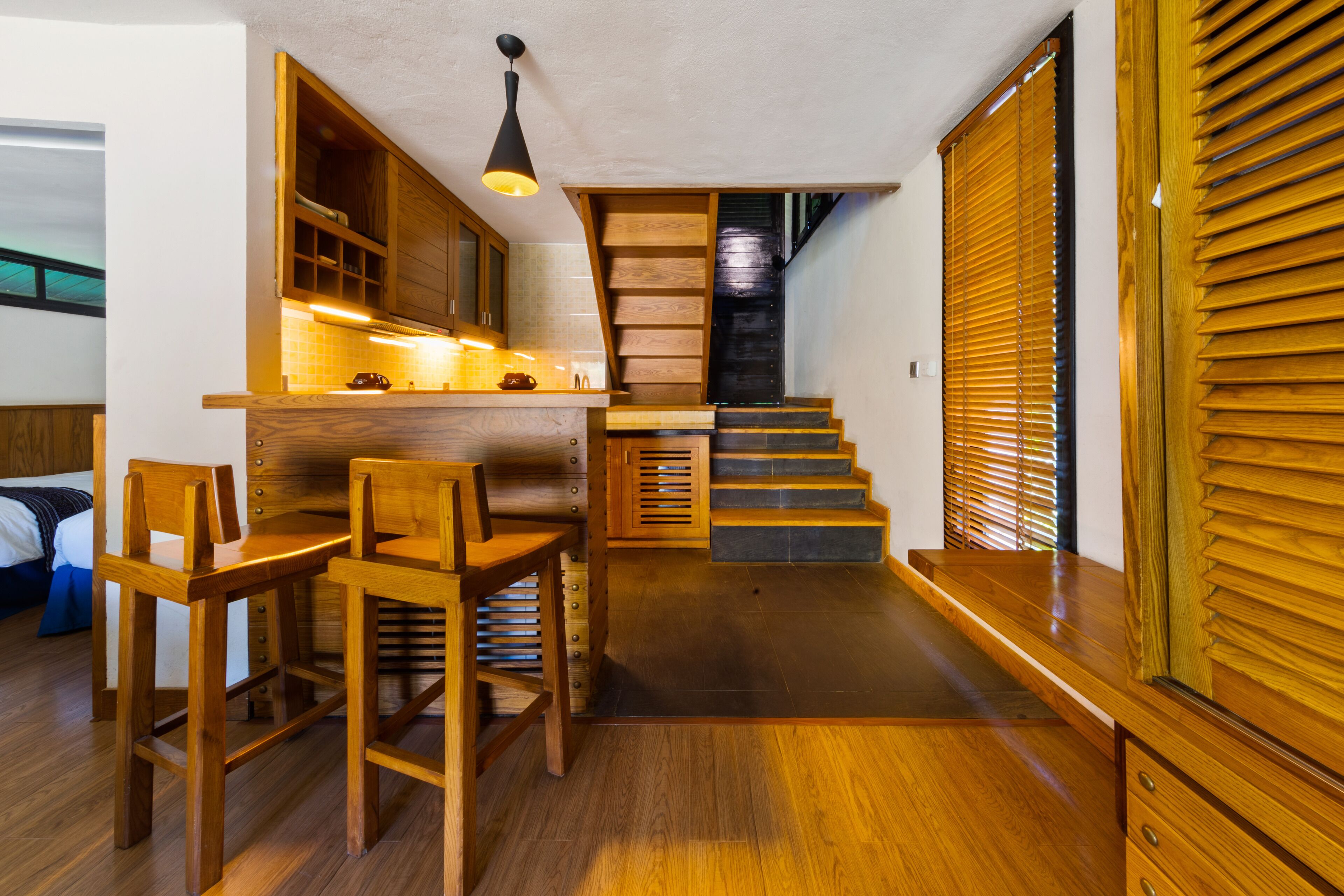 A modern kitchen with wooden cabinets, a bar area with stools, and a staircase leading to another level.