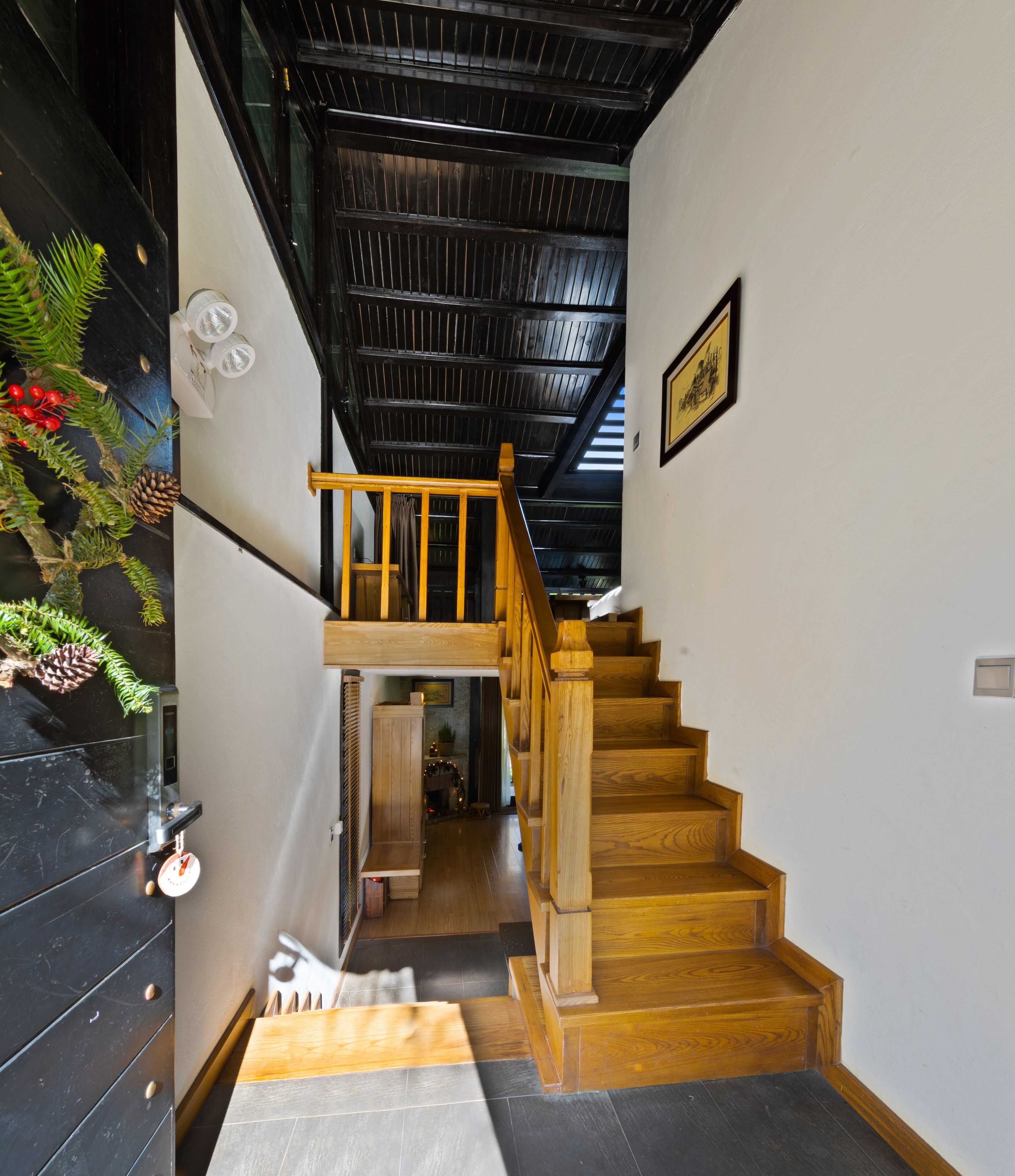 A staircase with wooden steps leading to a second-floor landing, a black wall with a decorative pine branch, and a ceiling with a grid pattern.