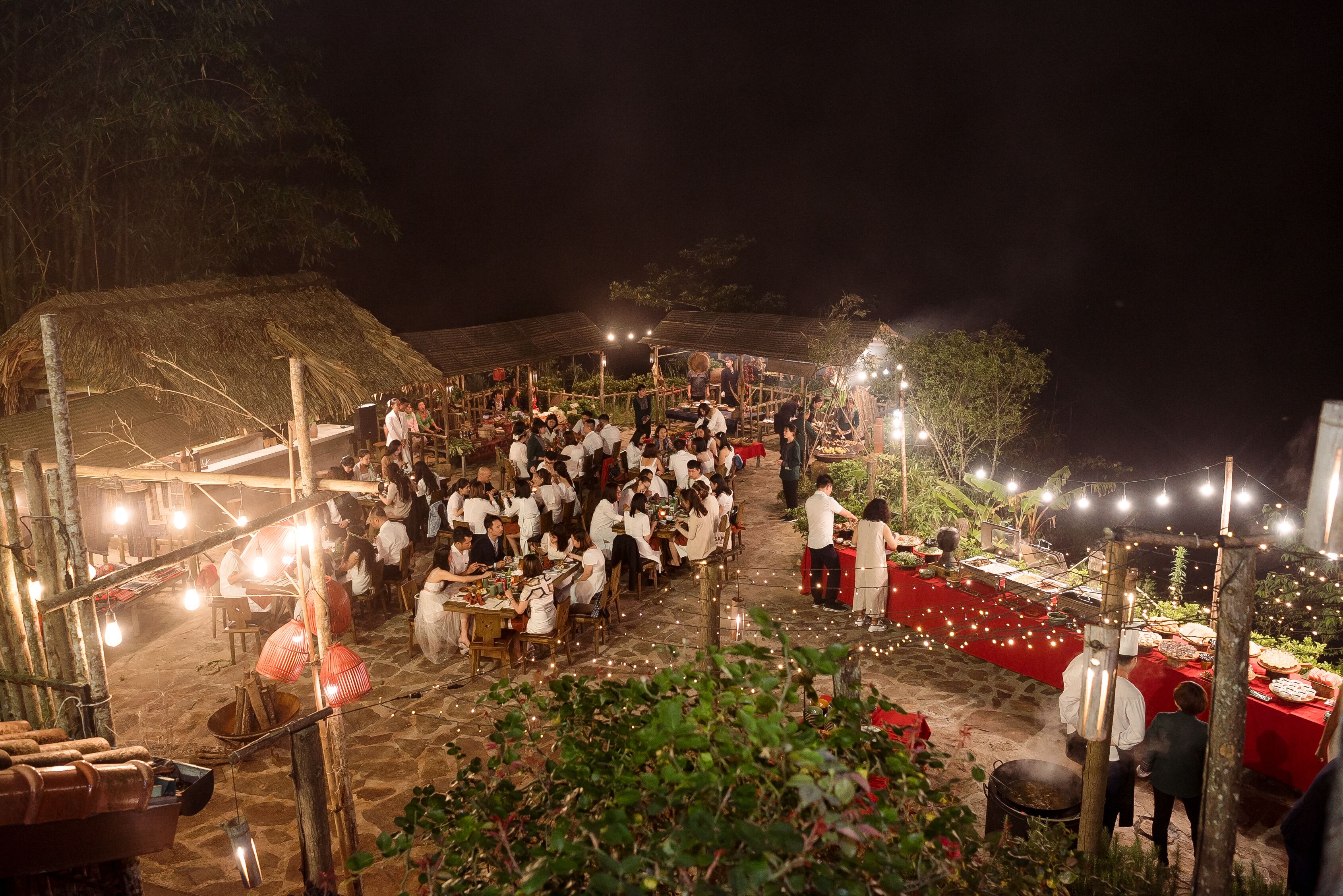 A crowded outdoor dining area with bamboo structures and string lights.