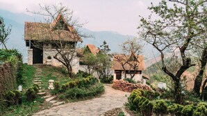 A stone pathway leading to traditional houses with tiled roofs, surrounded by lush greenery and mountains in the background. - Sapa Jade Hill Resort & Spa (Sa Pa)