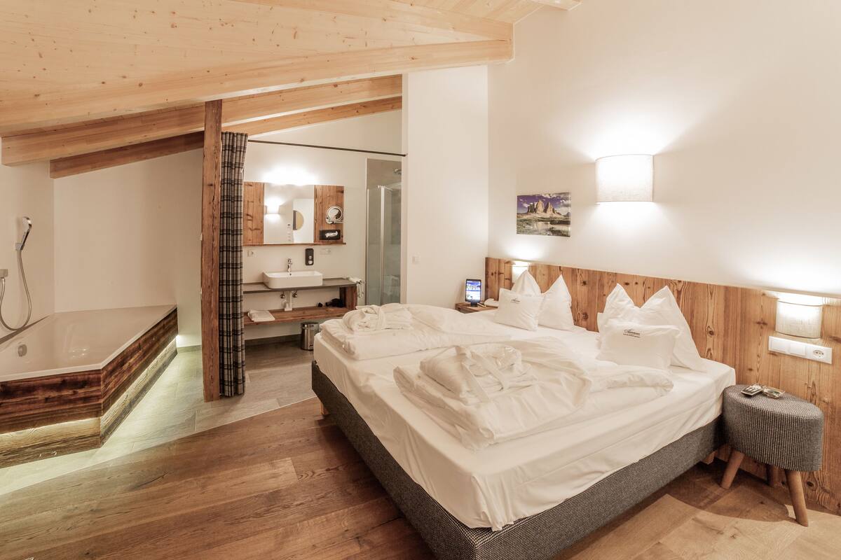 A modern bedroom with a large bed, wooden ceiling beams, a small bedside table, and a shower area.