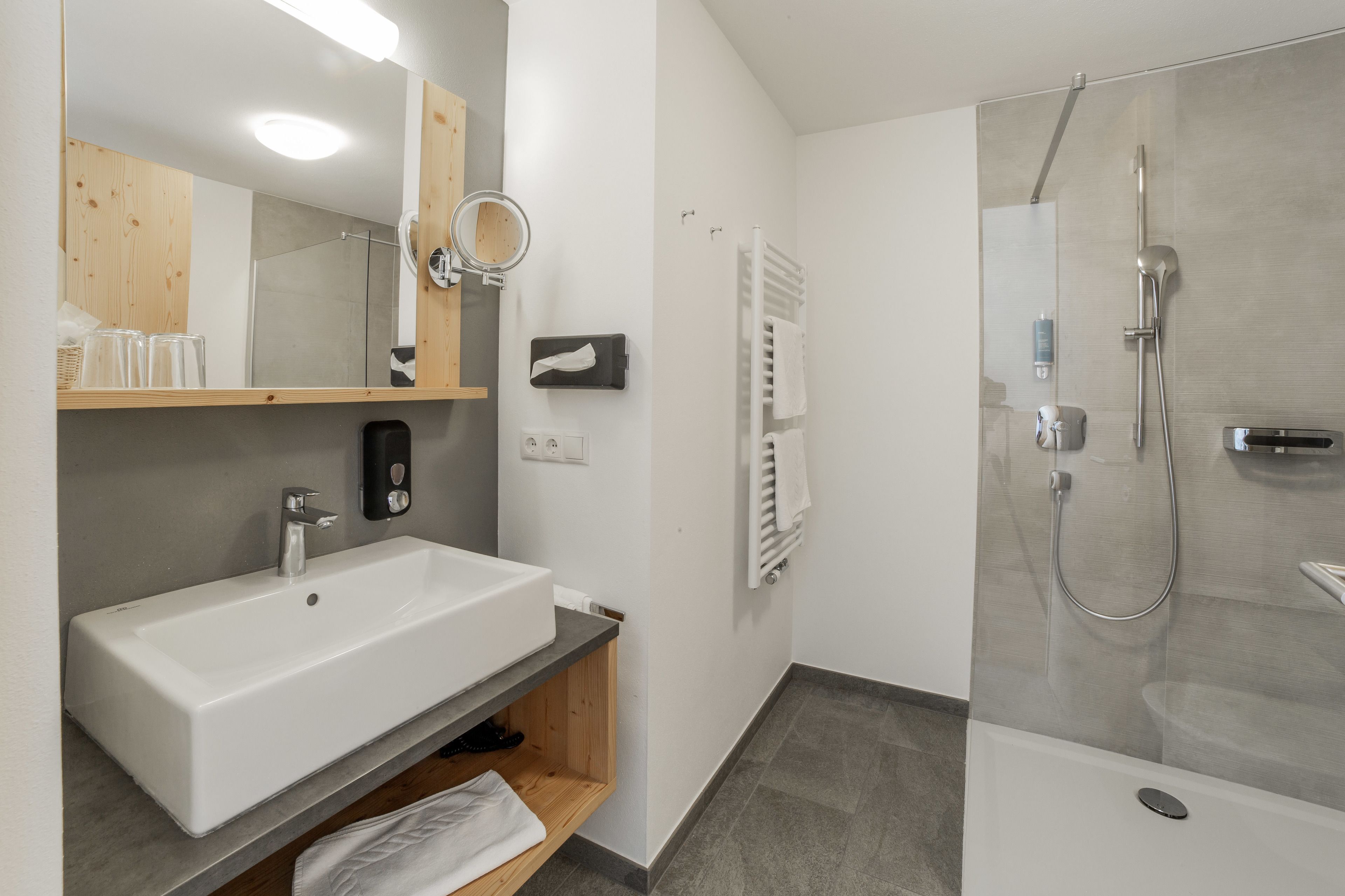 A modern bathroom with a large white sink, a mirror, a glass-enclosed shower, and a towel rack.