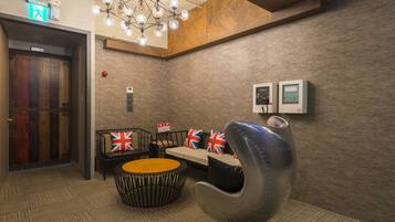 A modern lobby with a wooden door, a seating area with British flags, a unique metal chair, and a ceiling light fixture.