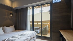Une chambre d’hôtel comprenant un lit, une table en bois, une chaise et une porte-fenêtre coulissante donnant sur un espace extérieur avec une terrasse en bois et une table.