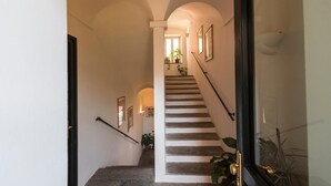 Un escalier muni d’une rampe, menant à un palier avec une fenêtre et des plantes en pot.