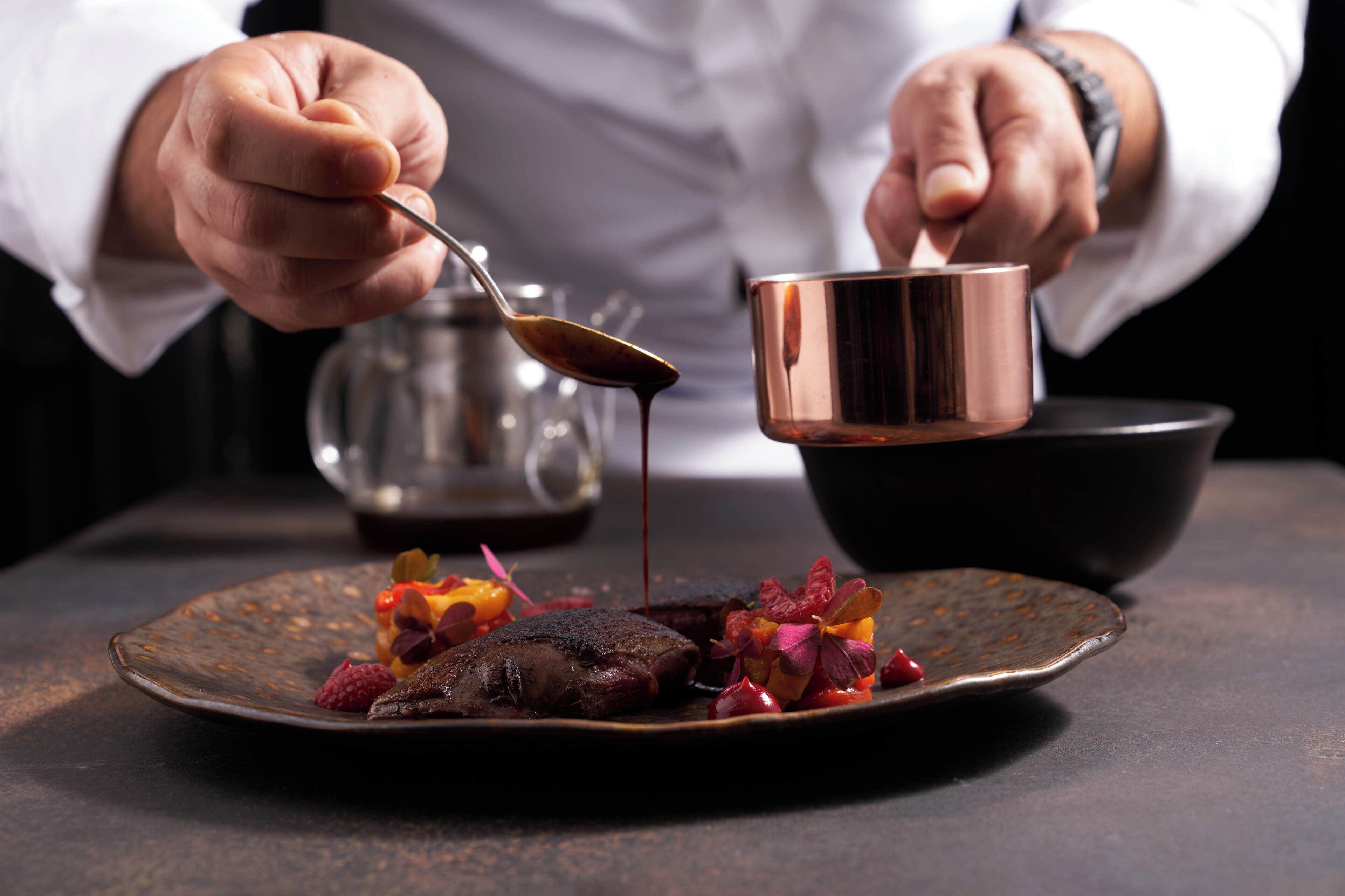 A person pouring sauce over a dish of food on a plate.