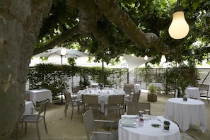 An outdoor dining area with round tables and chairs, covered by white canopies, and surrounded by greenery. - Hôtel Restaurant Claude Darroze (Langon)