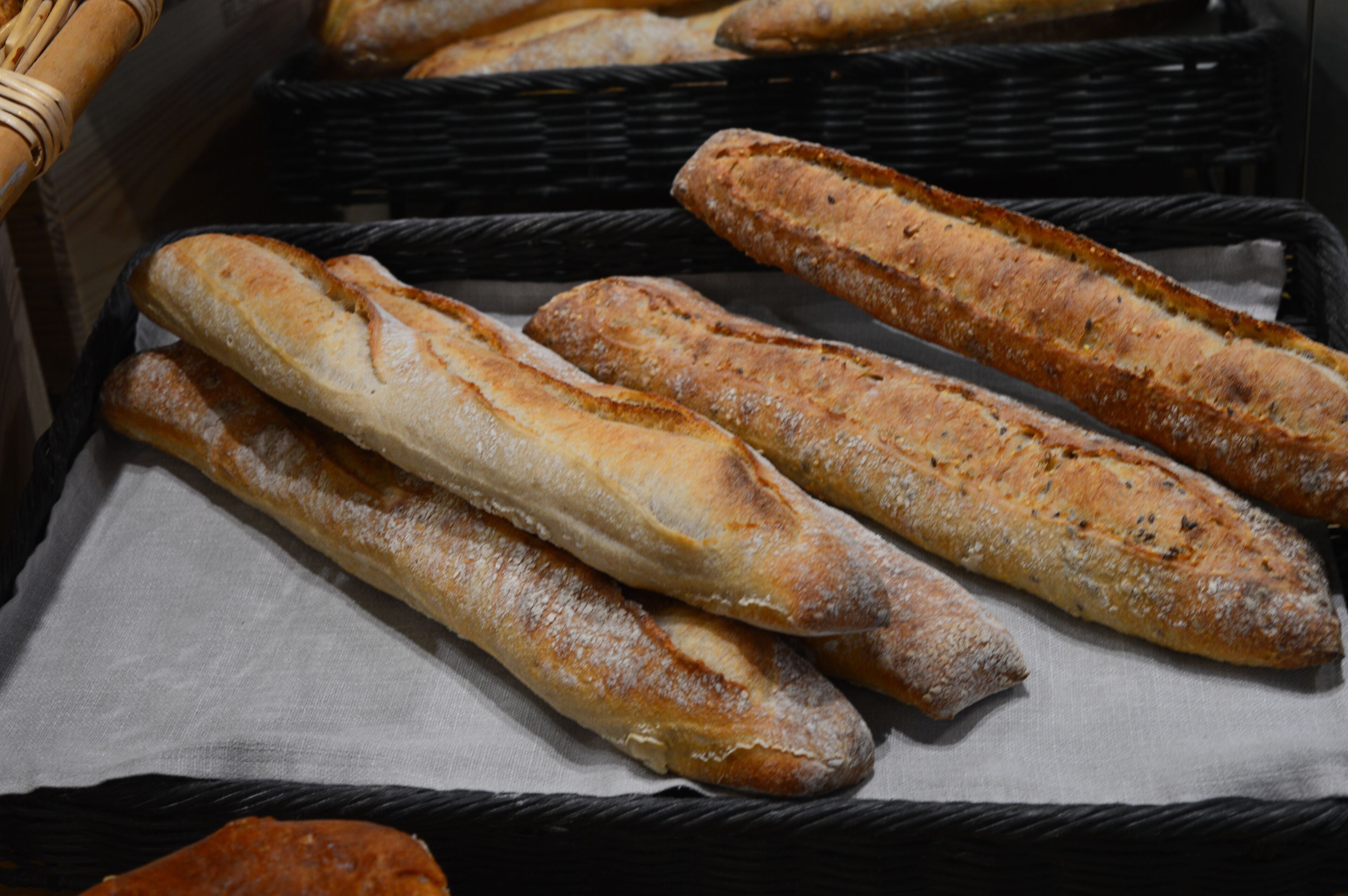 A basket containing several baguettes on a white cloth.