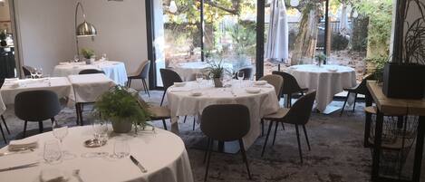 A dining area with round tables, chairs, and potted plants.