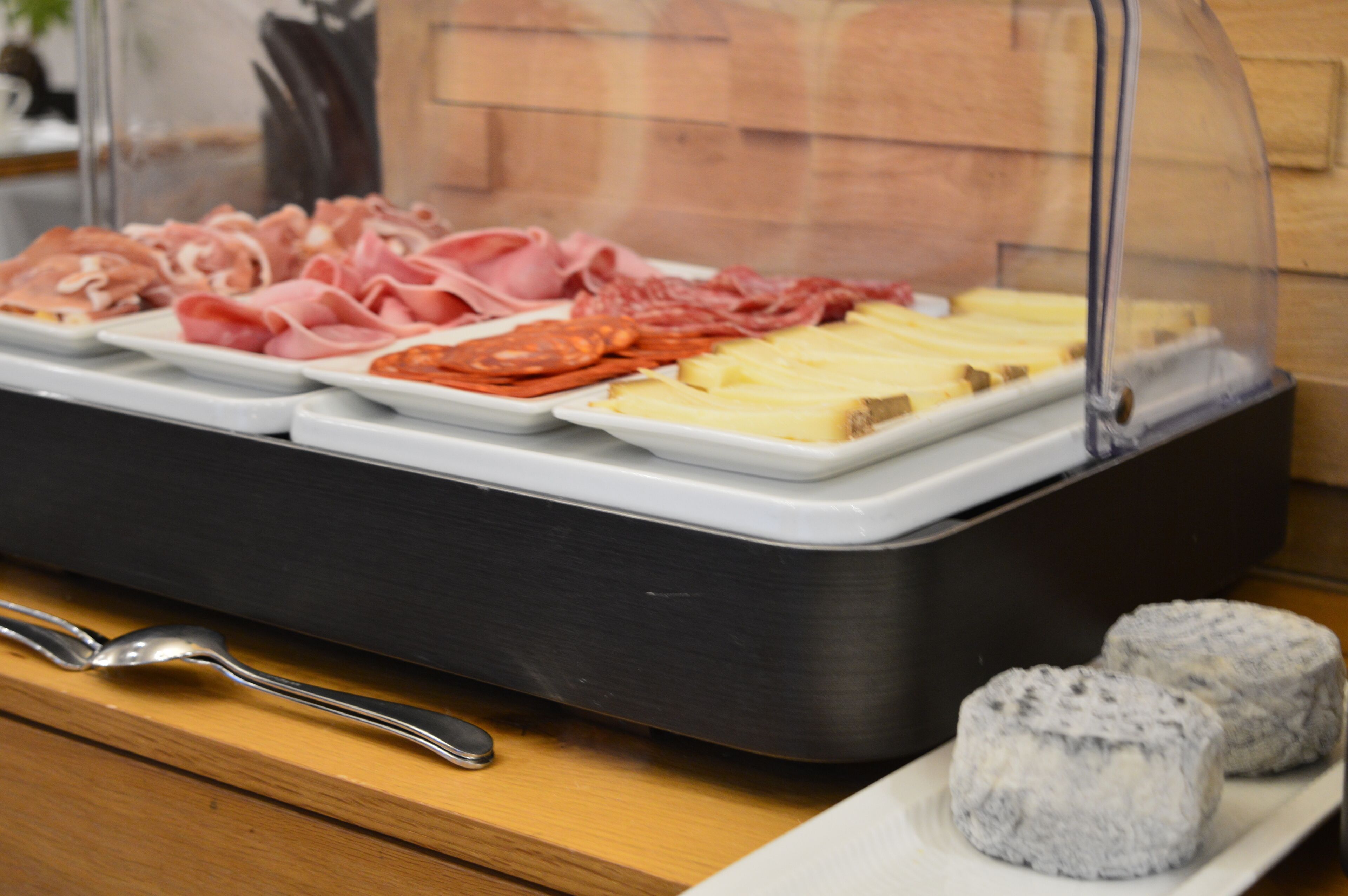A food display with various meats and cheeses, a spoon, and two round pastries on a wooden table.