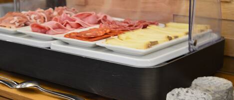 A food display with various meats and cheeses, a spoon, and two round pastries on a wooden table.