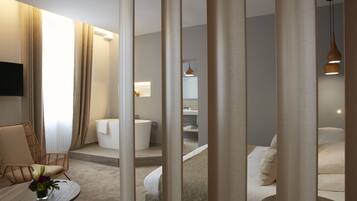 Una habitación de hotel moderna con una cama, un área de descanso con una mesa y una silla, una bañera y un baño pequeño.