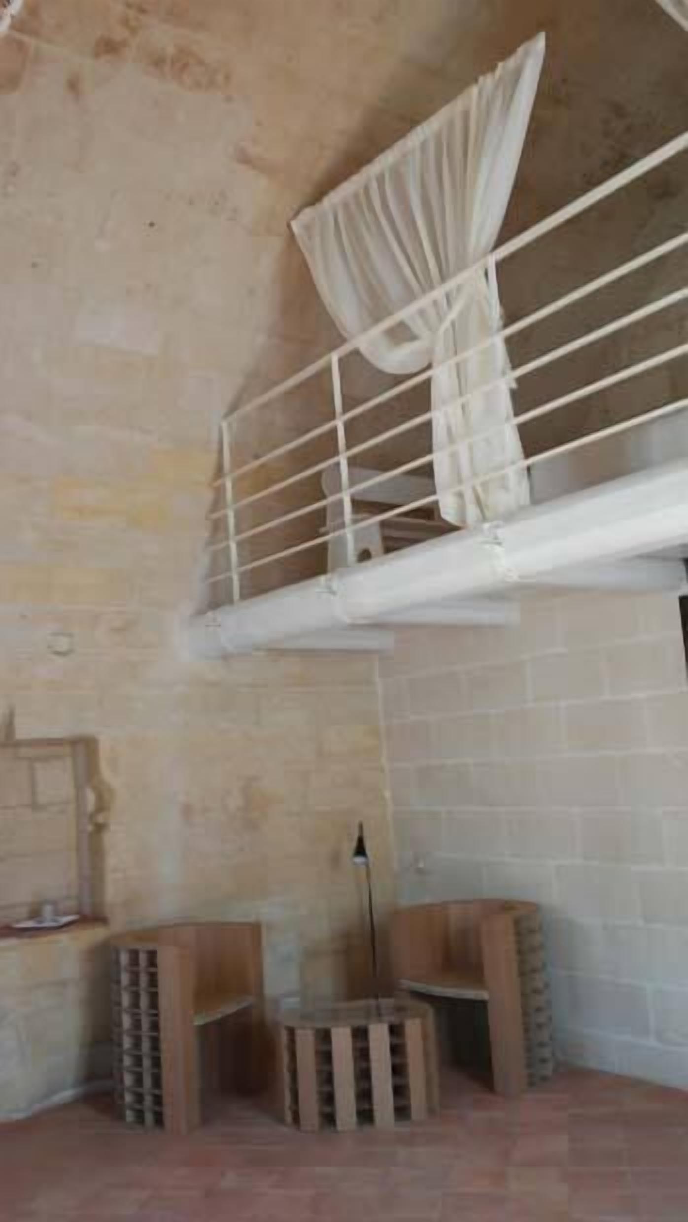 Une pièce avec un mur en briques, une rambarde blanche et un rideau. On y trouve des caisses en bois et un présentoir en métal dans un coin.