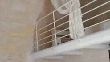 Une pièce avec un mur en briques, une rambarde blanche et un rideau. On y trouve des caisses en bois et un présentoir en métal dans un coin.