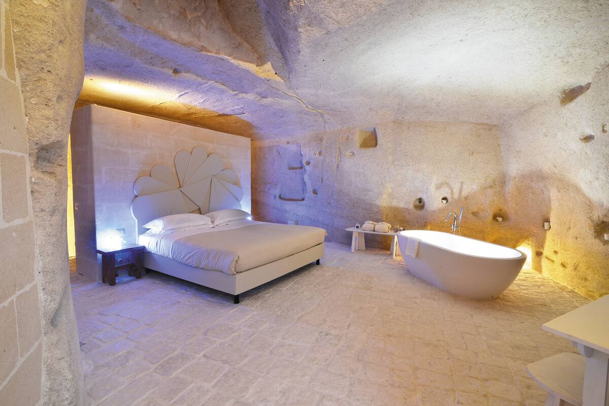 A bedroom with a large bed, a bathtub, and a small table.